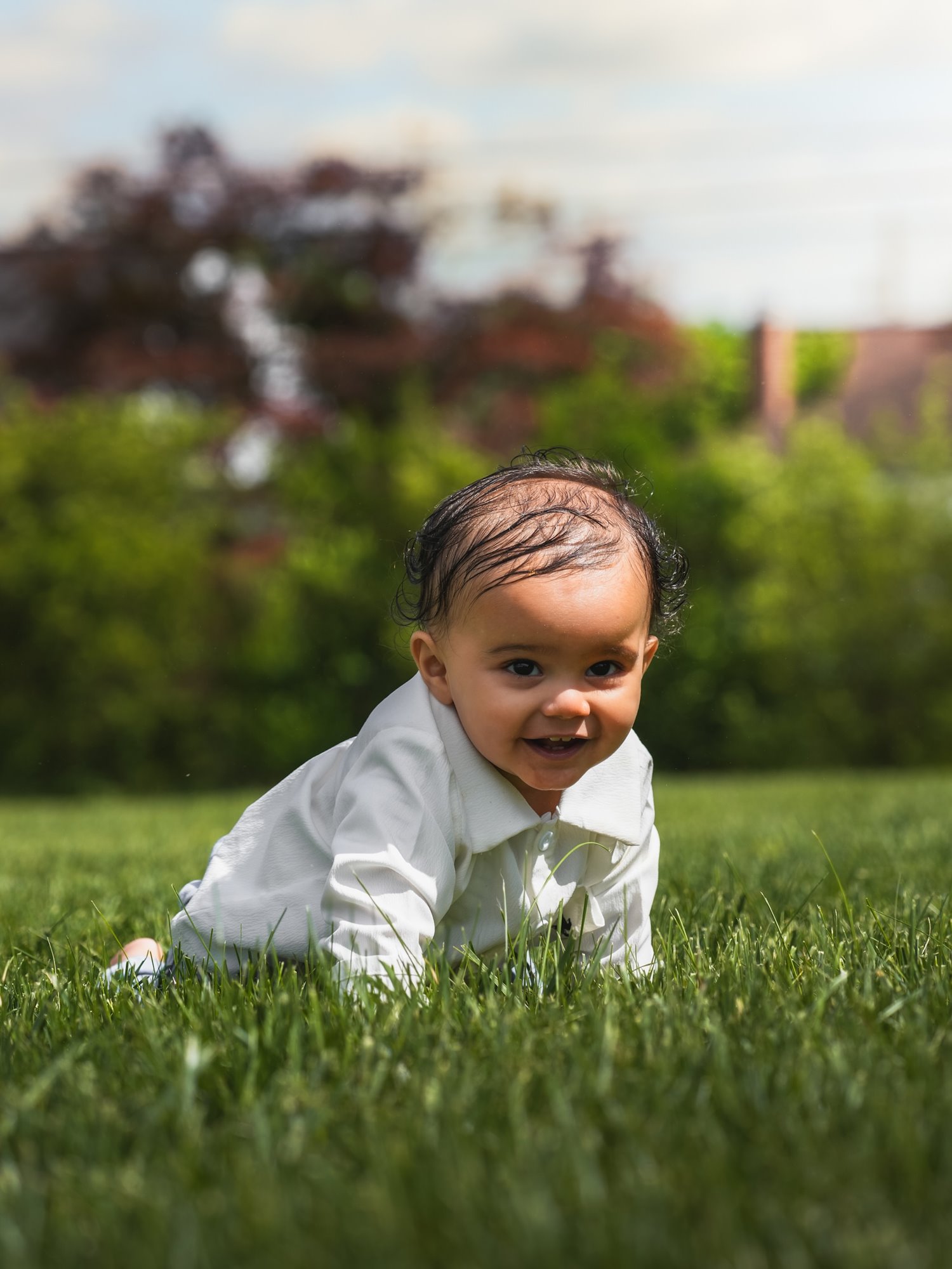 A smiling baby in a white shirt crawling across the grass