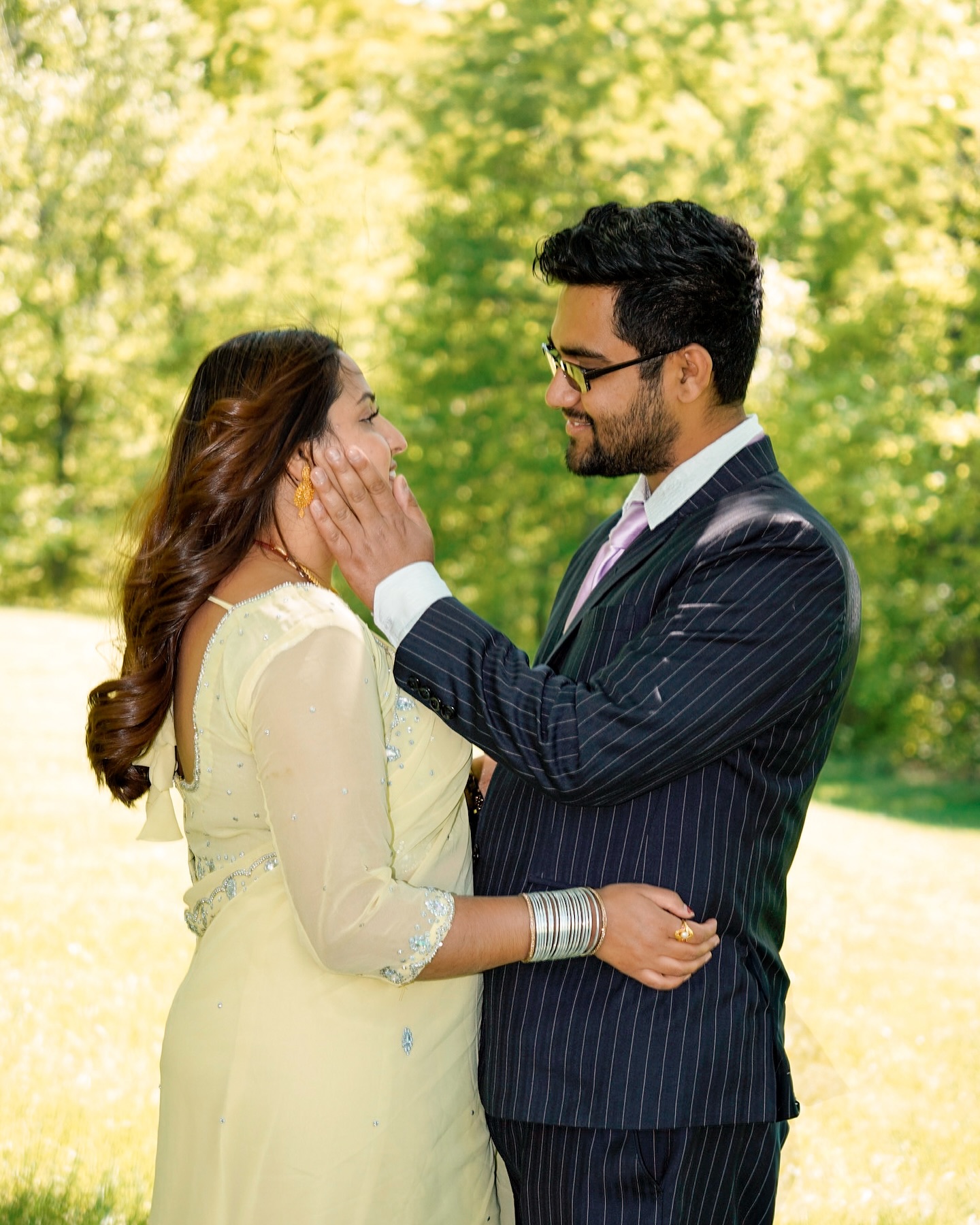 A man in a pinstripe suit holding his partner's face in a sunny park, both smiling