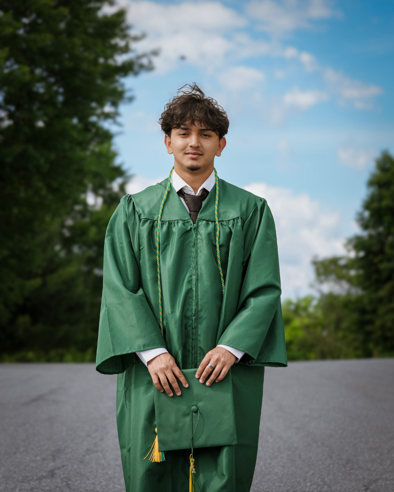 A graduate in a green gown holding his cap in both hands