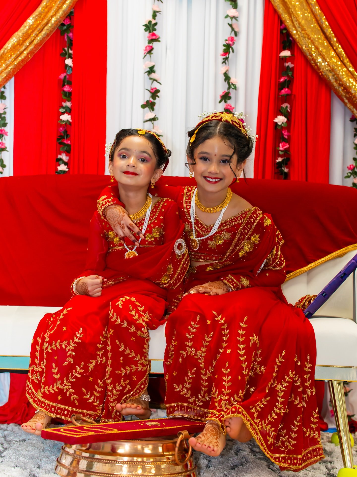Two young sisters in red and gold Gunyu Cholo sitting side by side on a white sofa