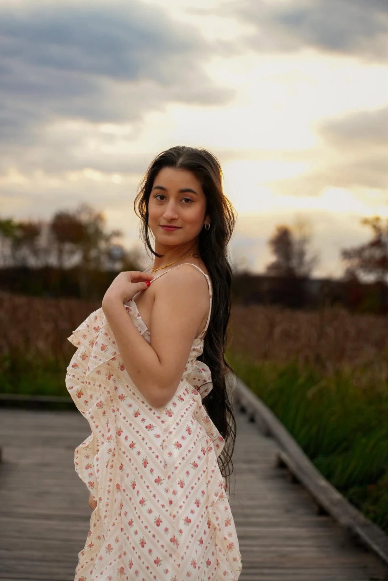 A woman in a floral dress looking over her shoulder on a boardwalk at sunset