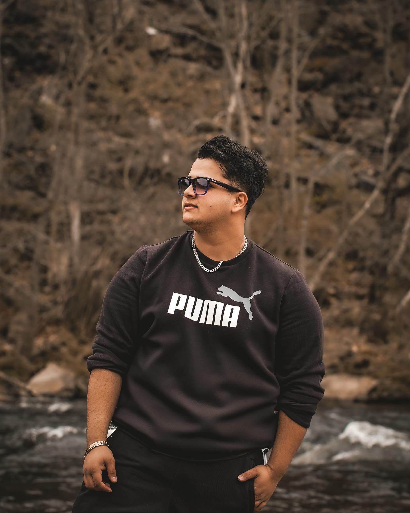 Prakash Timsina standing beside a river in a black sweatshirt and sunglasses, looking to one side