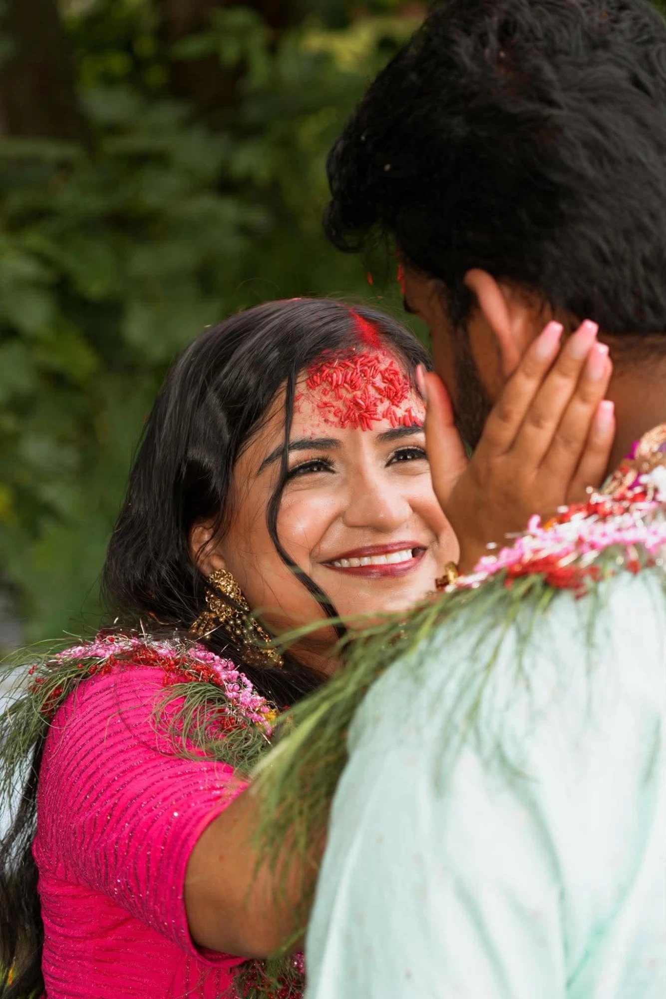 A bride with red tika on her forehead smiling up at the groom, her hand on his cheek
